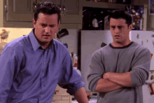 two men are standing in a kitchen with their arms crossed .