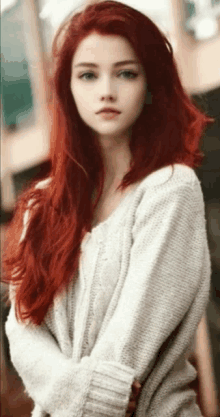 a woman with long red hair and blue eyes is wearing a white sweater