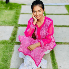 a girl in a pink and white dress is sitting on a sidewalk with her hand on her chin