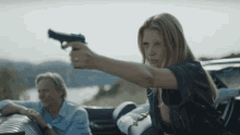 a woman is pointing a gun at a man in a convertible