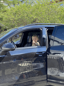 a little boy sits in the driver 's seat of a black suv