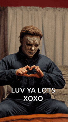 a man in a mask is making a heart shape with his hands with the words " luv ya lots xoxo " below him