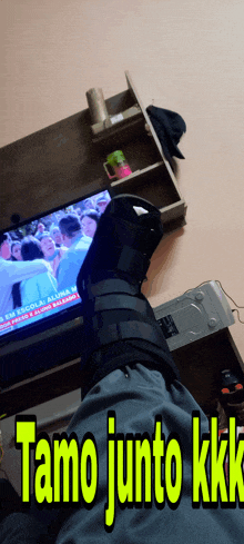 a person with a broken leg is sitting in front of a tv with the words tamo junto kkk written on the bottom