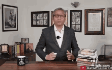 a man in a suit is standing in front of a table with a stack of books on it .