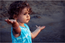 a little girl with curly hair is standing on the beach with her hands outstretched