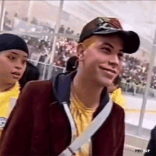 a man wearing a baseball cap and a yellow shirt is smiling while standing in front of a crowd .