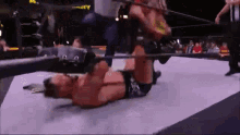 a wrestler is laying on the ground in a wrestling ring while a referee watches .