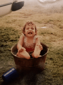 a little girl is sitting in a bucket of water with her mouth open