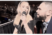 a woman is holding a microphone and talking to a man with a beard