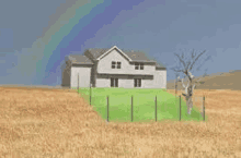 a house in the middle of a field with a rainbow in the background .