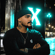 a man with a tattoo on his neck is standing in front of a neon sign that says x