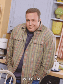 a man in a plaid shirt is standing in a kitchen with his hands in his pockets and welcom written on the bottom