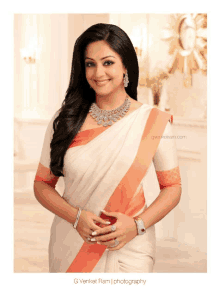 a woman wearing a white and orange striped saree is smiling for the camera