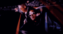 a man wearing sunglasses is being held by another man in a dark room