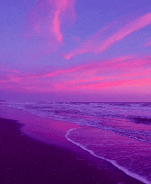 a purple sunset over a beach with waves crashing on the sand