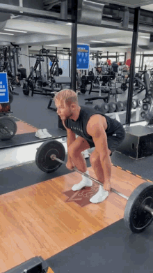 a man lifts a barbell in a gym while wearing a black tank top that says ' alpha ' on it