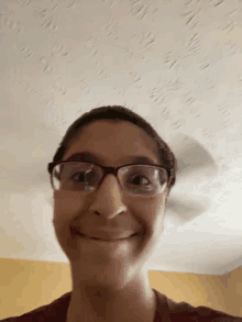 a woman wearing glasses and a maroon shirt is smiling in front of a ceiling fan