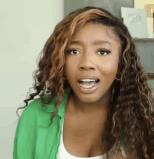 a woman with curly hair is wearing a green shirt and a white tank top