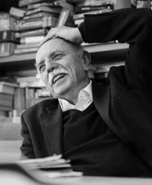 a man with a mustache is smiling in front of a shelf full of german books