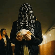 a person with a scarf on their head is holding a bunch of money in their hands .