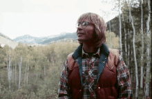 a man wearing glasses and a plaid shirt is standing in the woods