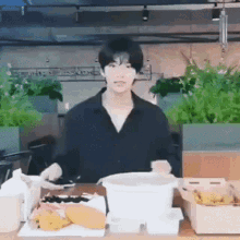 a man in a black shirt is standing in front of a table with a bowl of food on it .