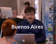 a man with a mustache is sitting in front of an apple laptop with the words buenos aires above him