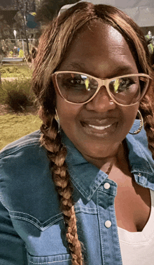 a woman wearing sunglasses and a denim shirt is smiling