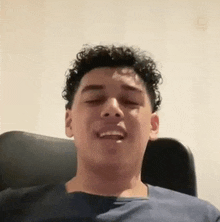 a young man with curly hair is smiling while sitting in a chair .