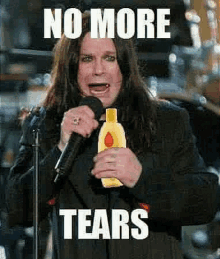 a man with long hair is singing into a microphone while holding a bottle of baby shampoo .