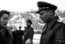 a black and white photo of a man in a military uniform talking to a woman in a crowd .