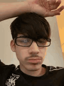 a young man with glasses and a mustache is making a funny face .