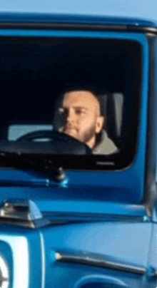 a man with a beard is driving a blue car