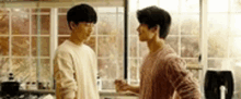 two young men are standing next to each other in a kitchen and talking to each other .