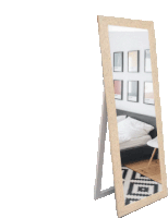 a full length mirror with a wooden frame shows a bedroom with a bed and chair