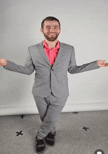 a man in a suit and a pink shirt stands with his arms outstretched