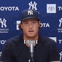 a man wearing a ny yankees hat is talking into a microphone while standing in front of a blue wall .