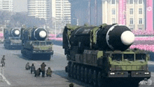 a group of military vehicles with missiles on them are driving down a street in a parade .