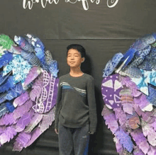 a young boy is standing in front of a wall with wings made of paper .