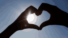 a person making a heart shape with their hands with the sun shining through