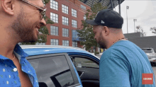 two men are standing next to a car with a subscribe button