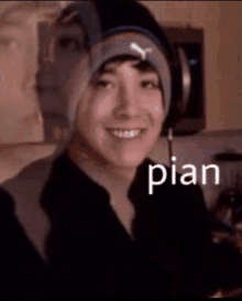 a man wearing a beanie and headphones is smiling and the word pian is on the bottom of his face .