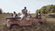 a man playing a guitar and a man playing a keyboard are sitting in the back of a truck in a field .