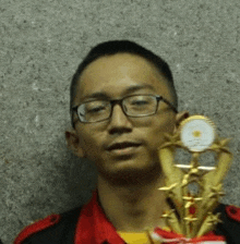 a man wearing glasses is holding a gold trophy .