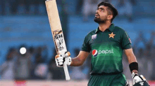 a man in a green shirt is holding a cricket bat in his hand .