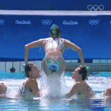 a group of synchronized swimmers are performing in a pool with rio 2016 written on the wall behind them .