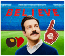 a man with a mustache is standing in front of a stadium with the words believe written on it .