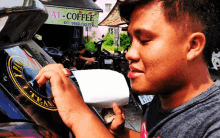 a young man is working on a motorcycle with a sign that says " at coffee " in the background