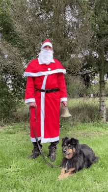 a man dressed as santa claus holds a bell next to a dog on a leash