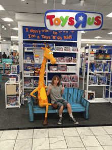 a boy sits on a bench in front of a toys r us store